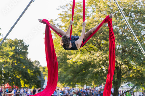 Young male aerial acrobatic dancer is is doing a split on a red ribbon