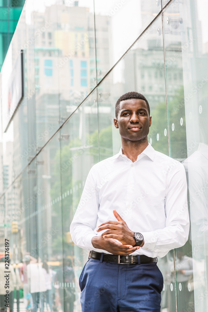 Young African American Man wearing white long sleeve shirt, blue pants,  wristwatch, standing against glass wall with reflections on street in  Manhattan, New York, looking around, relaxing, thinking.. Stock Photo |  Adobe