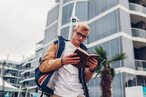 College student with backpack reading book walking by modern hotel on tropical beach photo