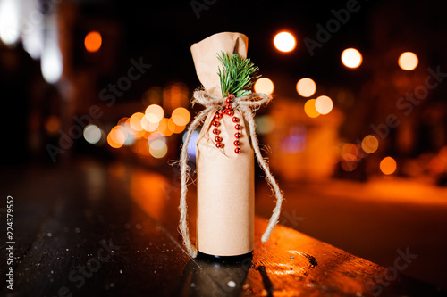 Adorable christmas decorated bottle with ribbon, fir-tree branch and beads in the craft paper