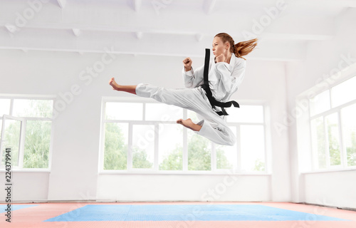 Woman in white kimono with black belt jumping and performing kick.