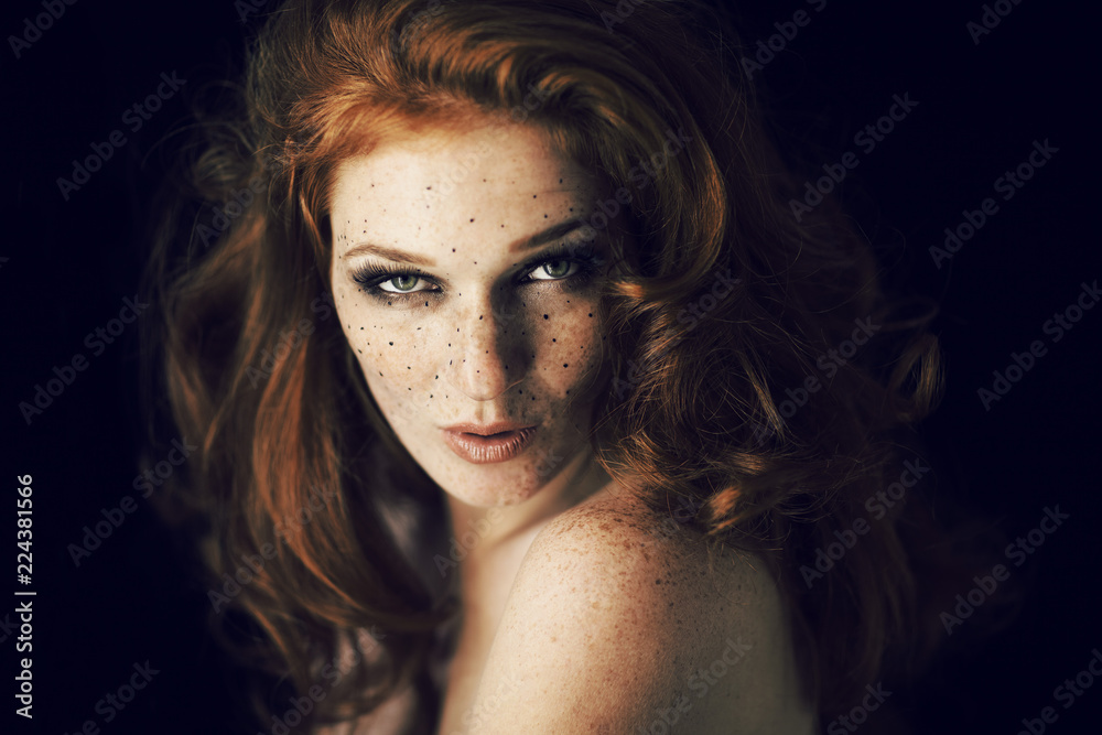 Beautiful young woman with red hair and freckles portrait, beauty shoot on dark background, mysterious dark mood