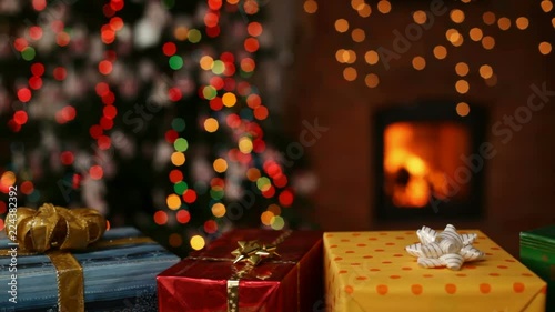 Many christmas gifts in front of fireplace and blurry lights on xmas tree in the evening - camera sliding