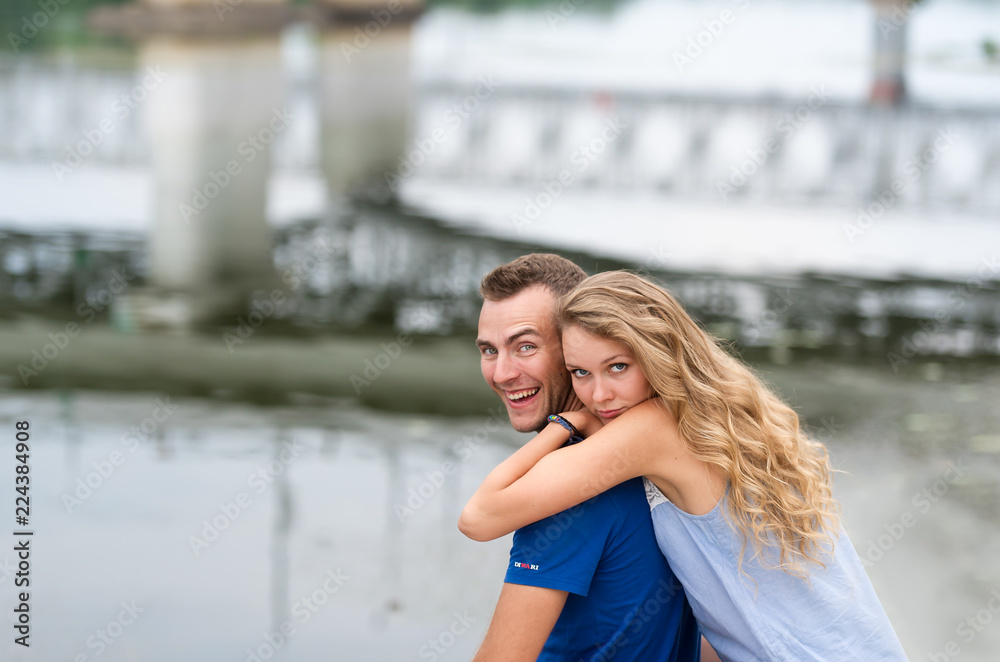 Happy couple hugging while sitting on the bank of the river on summer