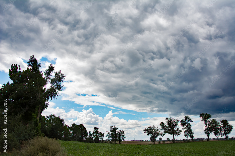 Dramatic grey clouds with a bit of blue sky and a green field and trees Dramatic grey clouds with a bit of blue sky and a green field and trees