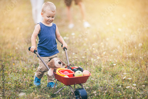 Child with his parents pushing a whellbarrow outdoors photo