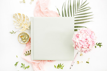 Composition with wedding or family photo album, hydrangea flower bouquet, tropical palm leaf, pastel pink blanket, gold monstera plate on white background. Flat lay, top view still life concept.