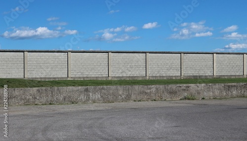 Urban street background. Am asphalt road in front of a long concrete brick wall under a blue sky with fluffy clouds