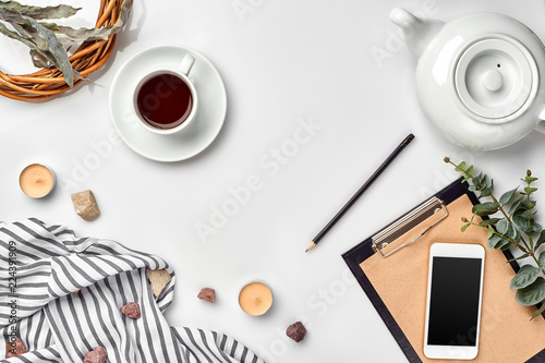 Notepad with pen and cup of tea on white table. Working space. Handmade. Top view, flat lay.