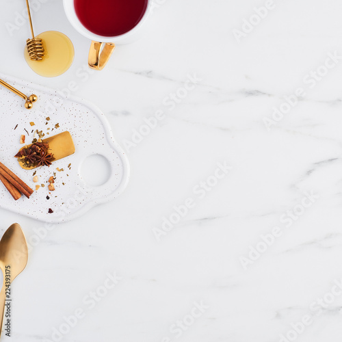Top view of white cup of tea, golden spoon, honey, herbs and tea mesure on serving plate. Cup of tea on white marble background with dried herbs. Flat lay.