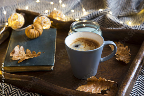 Cozy autumn setting with cup of cofee , book , candle and lights in a wooden tray