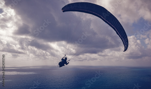 Silhouette of a man flying on a paraglider high above the sea in the clouds, sport, beauty and freedom concept