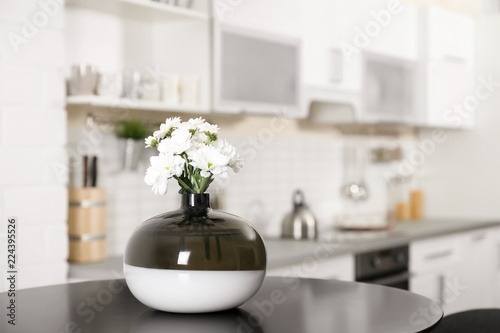 Vase with beautiful flowers on table in kitchen interior. Space for text © New Africa