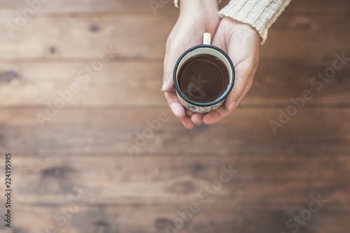 A girl in the winter knitted mittens with an iron mug of coffee on the wooden terrace. Winter concept