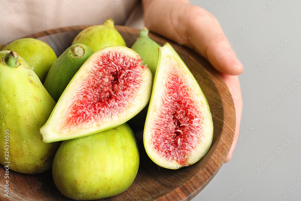 Woman holding bowl with fresh ripe figs on light background Woman holding bowl with fresh ripe figs on light background