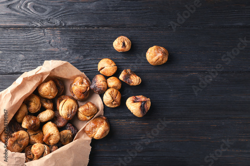 Paper bag with dried figs on wooden background, top view. Space for text