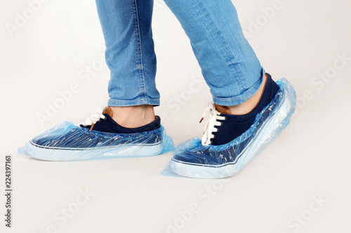 Fototapeta Naklejka Na Ścianę i Meble -  Man with blue shoe covers worn over sneakers on white background, closeup