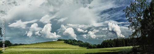 Scenic landscape with storm cloud in background over green agriculture fields,trees and meadows at spring daylight, dramatic clouds, sky.Relaxing nature,sunshine.Panoramic photo.Czech Repulic, Europe.