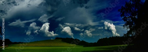 Scenic landscape with storm cloud in background over green agriculture fields,trees and meadows at spring daylight, dramatic clouds, sky.Relaxing nature,sunshine.Panoramic photo.Czech Repulic, Europe.