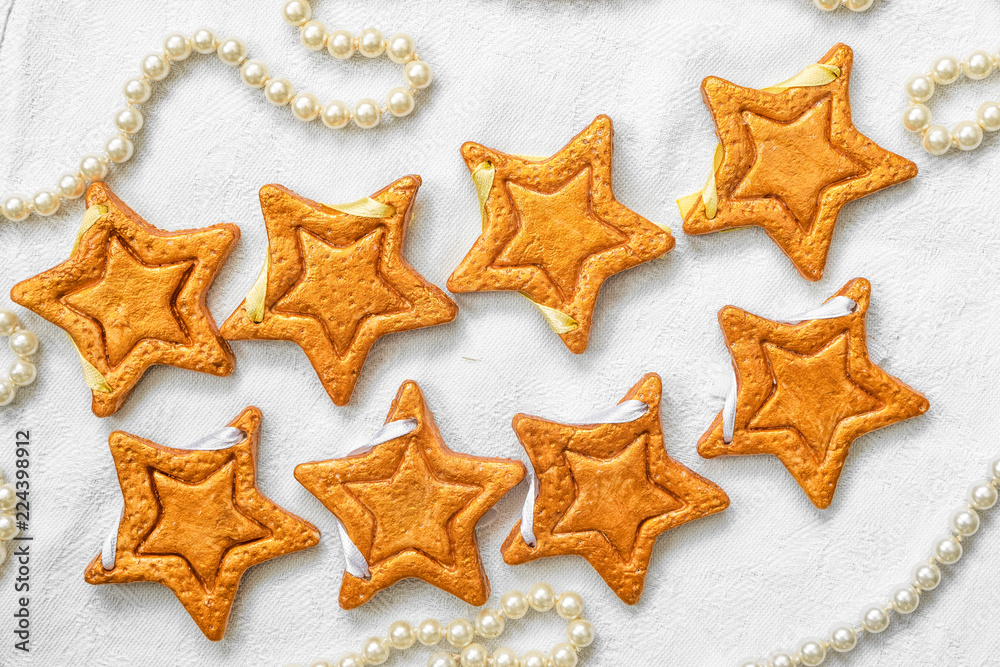 Two rows of eight decorative golden stars handmade from dough on a bright white fabric surface with pearl necklace Two rows of eight decorative golden stars handmade from dough on a bright white fabric surface with pearl necklace