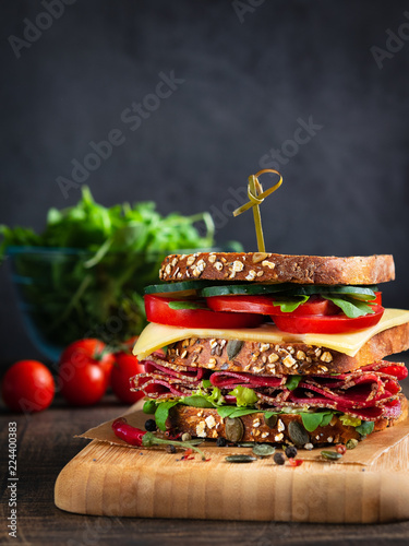 Close-up of delicious Sandwich with salami, cheese and fresh vegetables on rustic wooden cutting board on wooden table, selective focus. Space for text. Vertical. Club sandwich concept.
