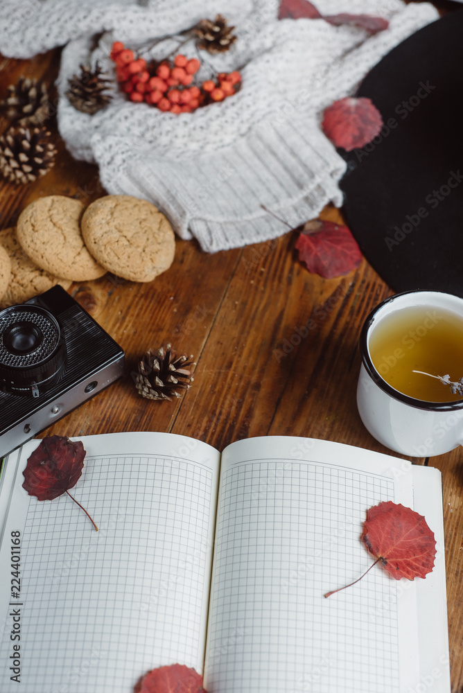  Flat lay view of autumn leaves and tartan textured sweater on wooden background with cup of tea . Autumn or Winter concept.