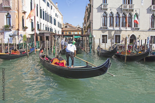 Venetian gondolier in the gondola is transported tourists through canal waters of Venice Italy