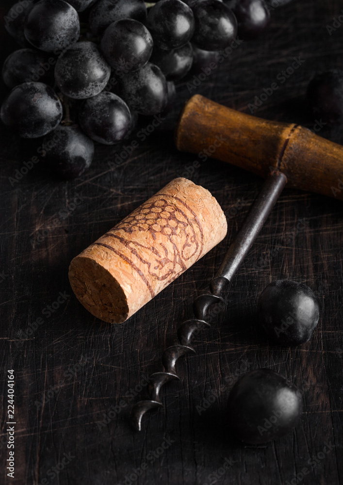 Vintage corkscrew opener with wine cork and dark grapes on wooden board