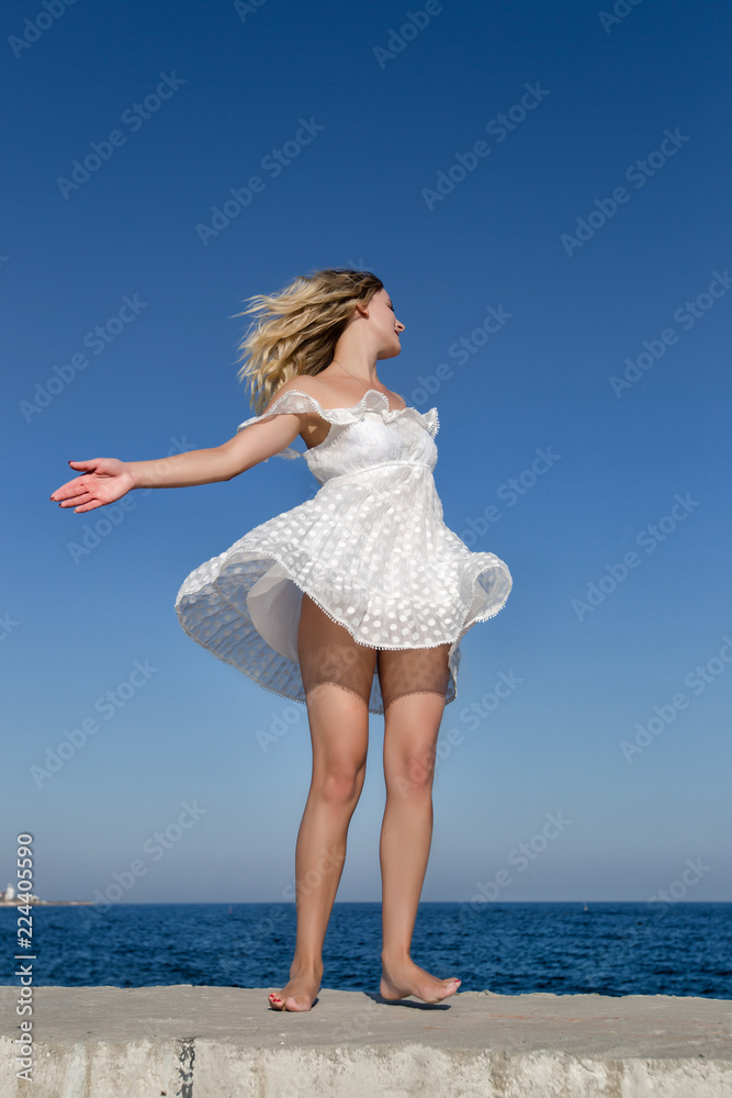 Barefoot girl in white dress whirls on seashore Barefoot girl in white dress whirls on seashore