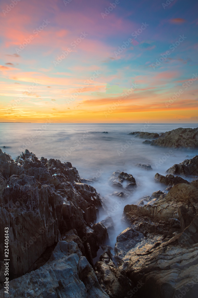 Obraz premium Long exposure seascape at sunset, Woolacombe, Devon, with milky seas washing over deformed slate coastal rocks from the Devonian period