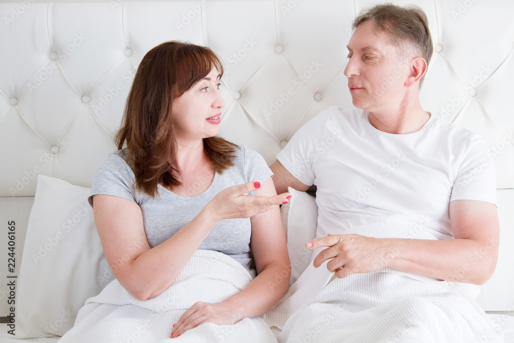 Middle age family couple talking in bed in the morning. Woman and man have dialogue. Healthy relationship. Love and romance
