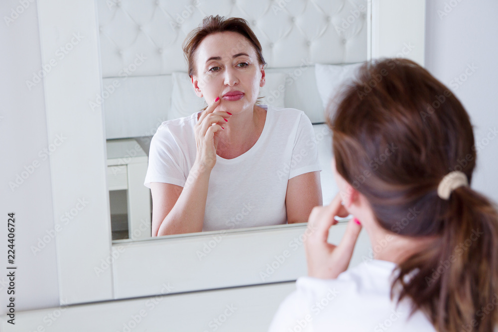 Middle age woman looking in mirror on face. Wrinkles and anti aging skin care concept. Selective focus Middle age woman looking in mirror on face. Wrinkles and anti aging skin care concept. Selective focus