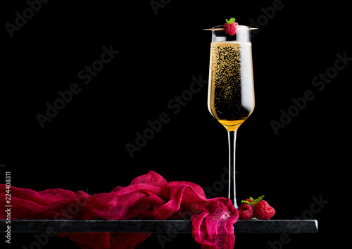 Elegant glass of yellow champagne with raspberry and fresh berries with mint leaf on stick on black marble board on black background.Space for text
