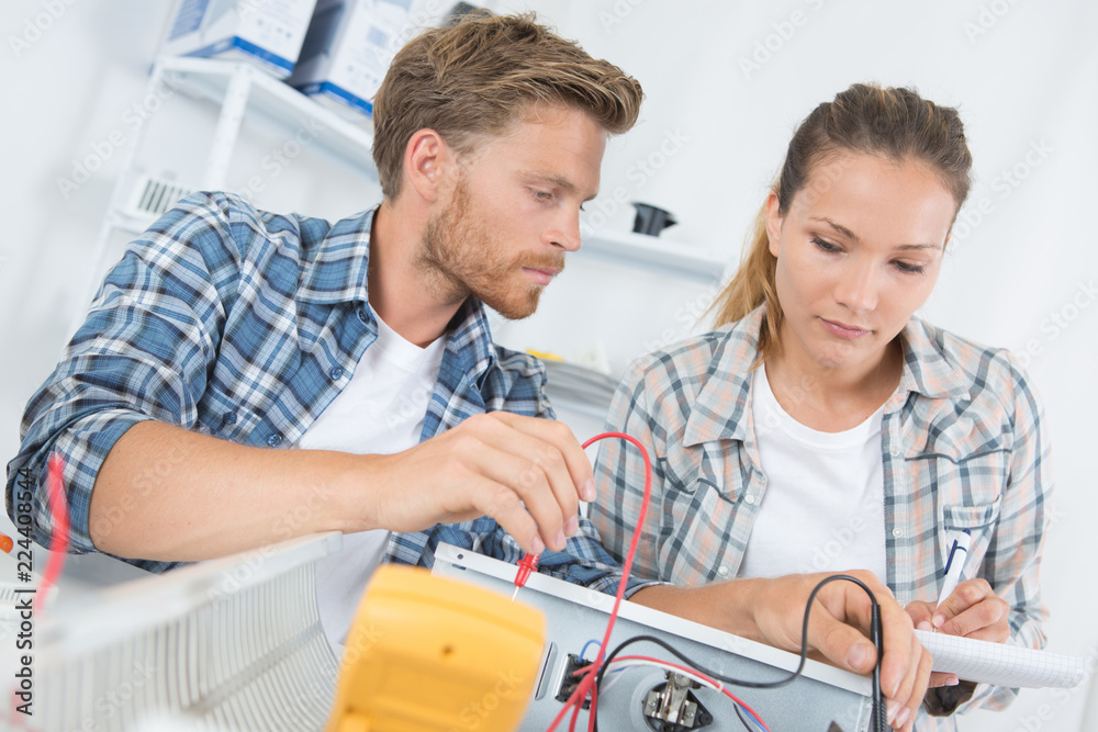 Fototapeta premium Two technicians testing appliance with multimeter
