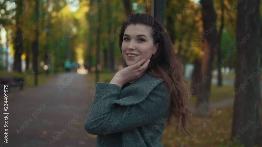 Amazing girl with curly hairstyle in coat walk in autumn alley, looking at camera and smiling in slow motion. Park and trees on background. Amazing girl with curly hairstyle in coat walk in autumn alley, looking at camera and smiling in slow motion. Park and trees on background.