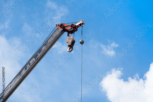 Mobile crane boom with hook hanging by wire cable background blue sky,close up
