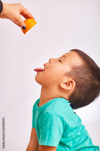 Child boy in a turquoise shirt, opened his mouth and stuck out his tongue, a female hand squeezes orange juice on the child's tongue - fruits and healthy food