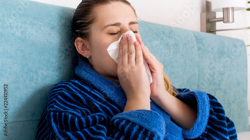 Принти на полотні Closeup portrait of young woman feeling unwell blowing nose in paper tissue