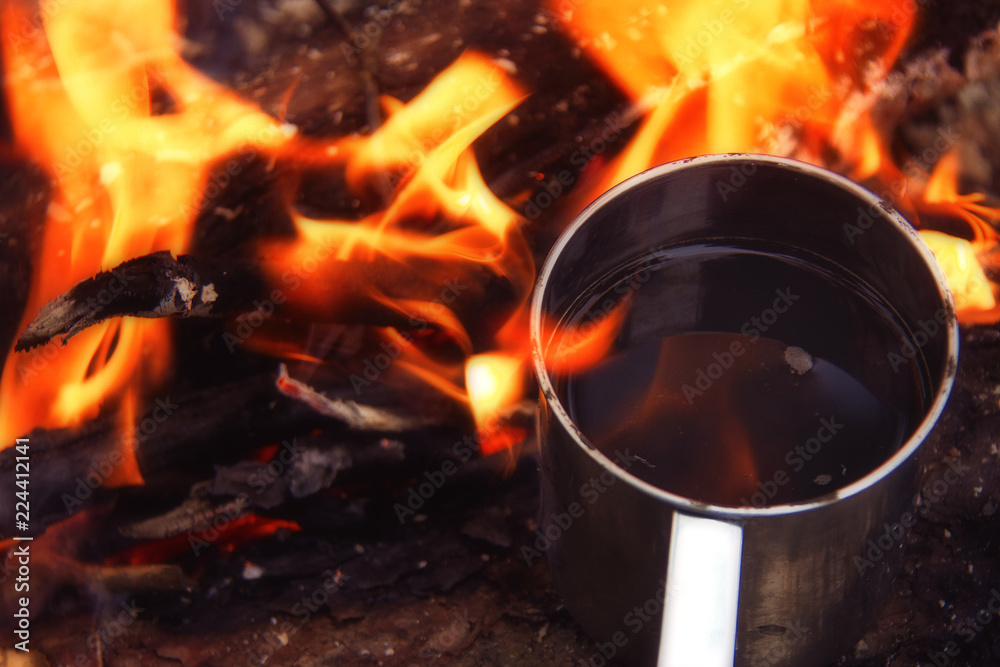 Tea or coffee in metal mug heats up on stone on bonfire. Hot drink on nature. Tea drinking in open air. Camping in dusk. Romantic warm atmosphere outdoor in twilight. Active rest Tea or coffee in metal mug heats up on stone on bonfire. Hot drink on nature. Tea drinking in open air. Camping in dusk. Romantic warm atmosphere outdoor in twilight. Active rest