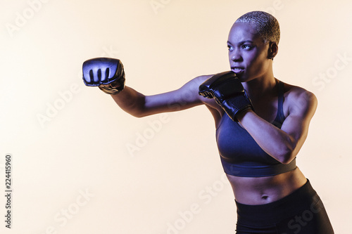 Pull a punch, portrait of a young woman boxing, against a blank studio background