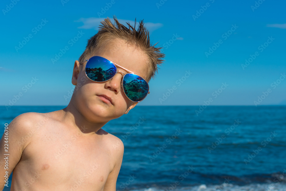 a beautiful little boy posing on a beach by the sea with sunglasses a beautiful little boy posing on a beach by the sea with sunglasses