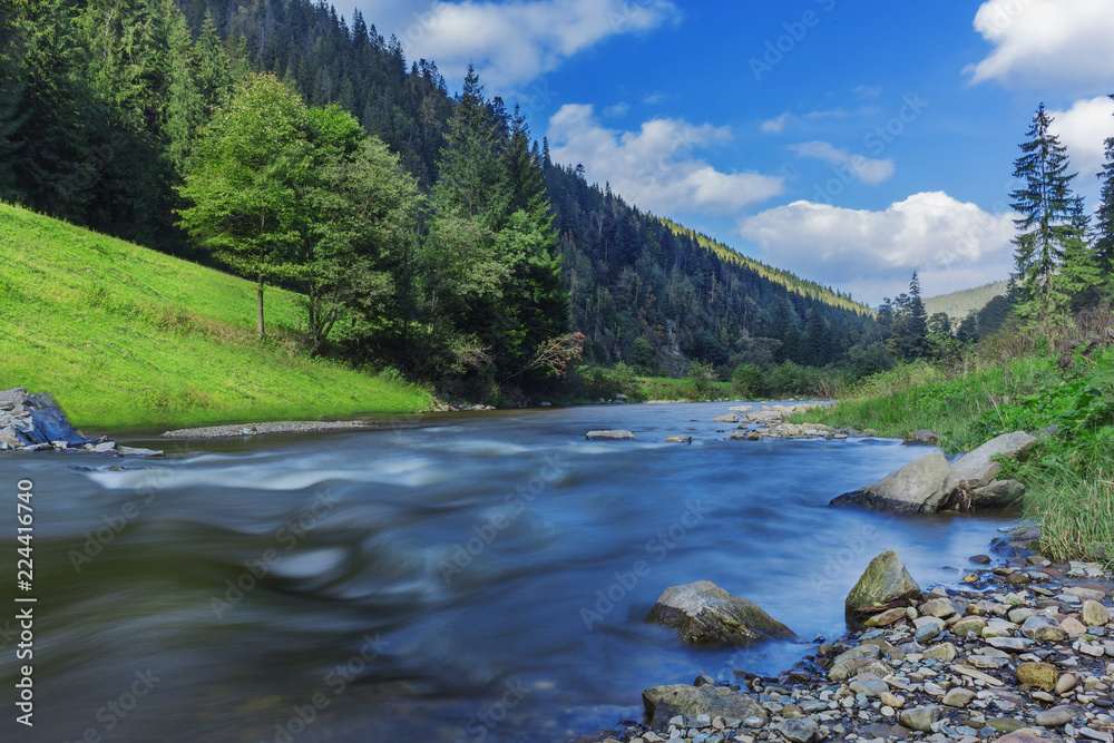 River in mountains with rocks,  green  grass on riverside. Mountain landscape, beautiful sky, clouds. Idea for outdoor activities, tourism, adventure. Blurred 