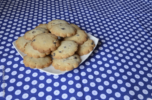 Homemade vanilla cookies with chocolate chips on white plate and blue tablecloth in Boleslawiec pottery pattern photo