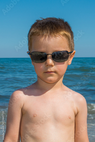 Konstfotografi a beautiful little boy posing on a beach by the sea with sunglasses