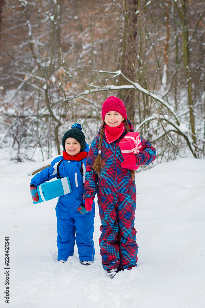Happy children in a winter snow-covered forest with gift boxes.