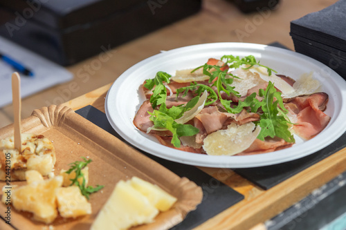 Street food cooking, demo cooking, catering service. Paper saucer with roast beef, pieces of parmesan, rucola leaves and olive oil. Summer street market menu.