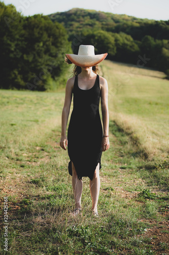 une femme  dans la campagne , en robe noire dont le visage est caché derrière un grand chapeau © Olivier Tabary