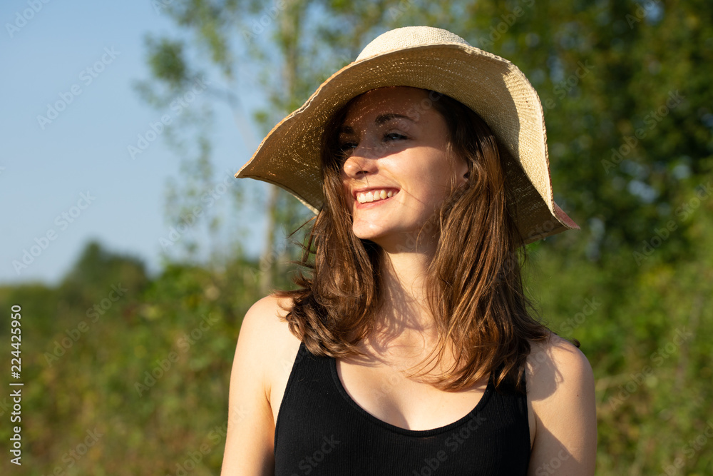 portrait d'une jeune femme souriante,  brune au cheveux longs en robe noire et un grand chapeau de paille