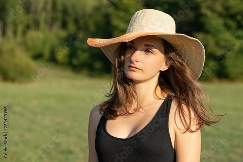 portrait d'une jeune femme brune au cheveux longs en robe noire et un grand chapeau de paille