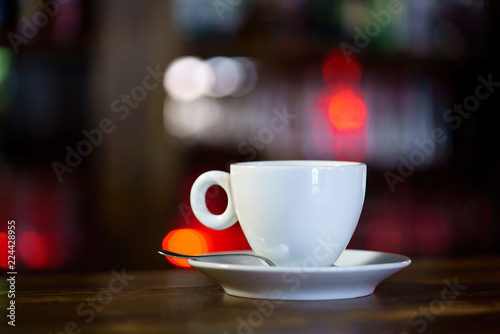 a white mug with a saucer and a spoon is on a wooden table in a restaurant. Close-up